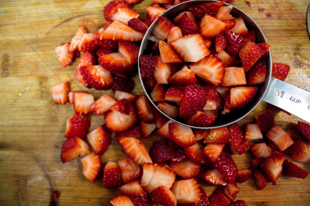 close up of diced strawberries in measuring cup on wooden cutting board