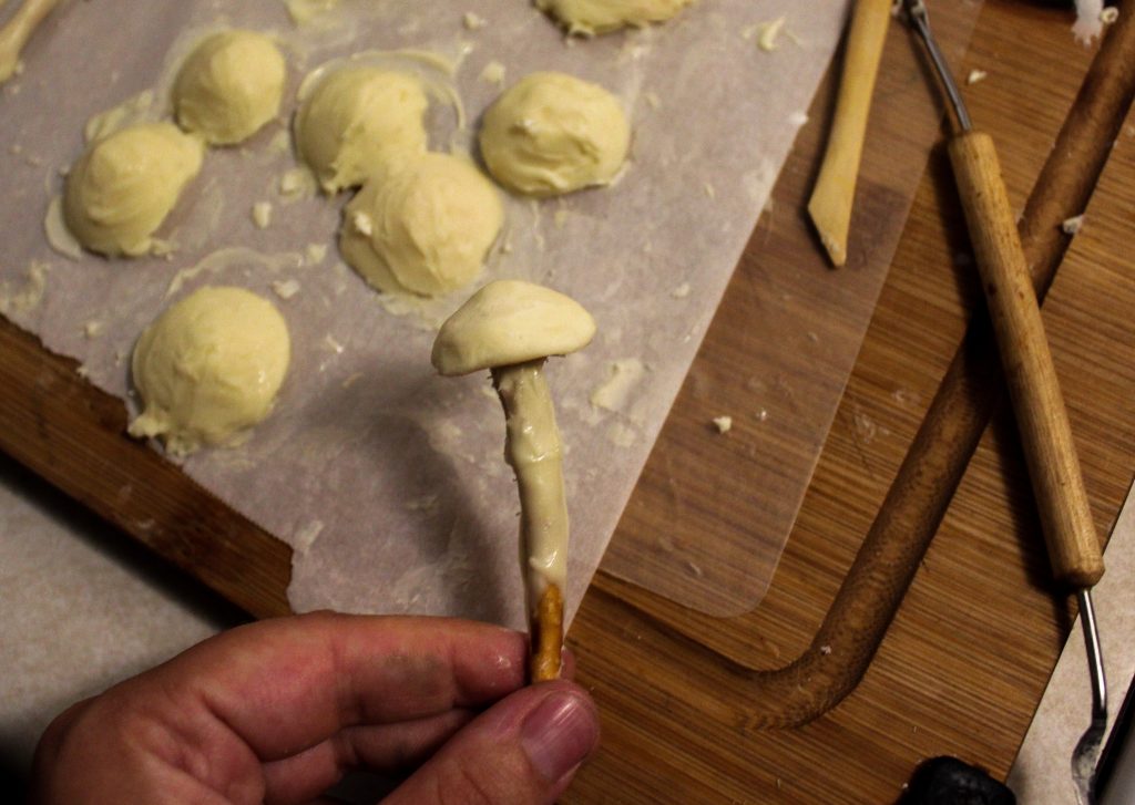 hand holding white chocolate mushroom with parchment paper and white chocolate in background